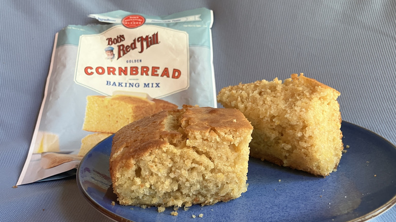 Two pieces of Bob's Red Mill cornbread on a blue plate with the cornbread mix packaging in the background.