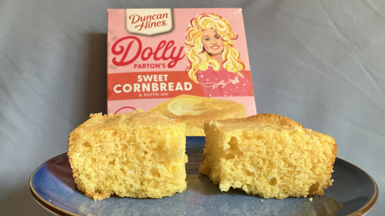 Two pieces of Duncan Hines Dolly Parton's Sweet Cornbread on a blue plate with the pink box of cornbread mix in the background.