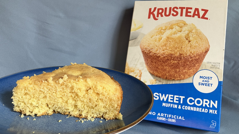 A wedge of Krusteaz Sweet Corn cornbread displayed on a plate next to the cornbread mix box.