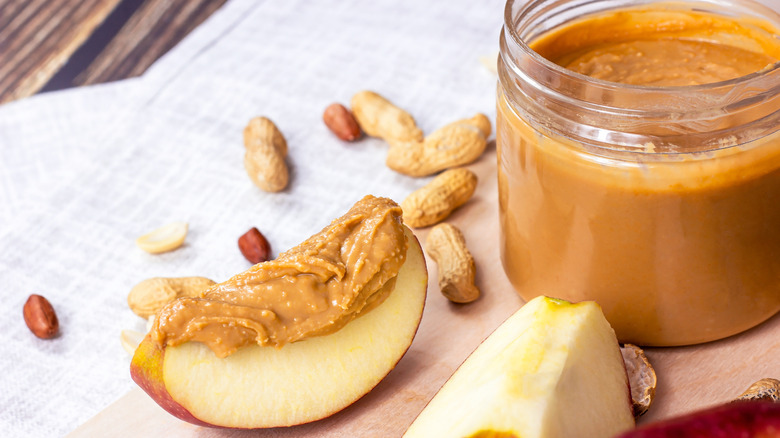 Apple slices with natural peanut butter on top next to plastic jar filled with peanut butter