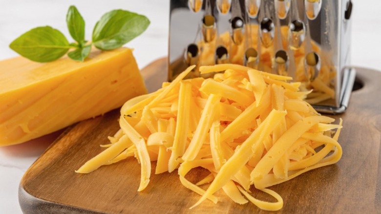 Close-up of shredded cheddar cheese next to grater and block of cheese