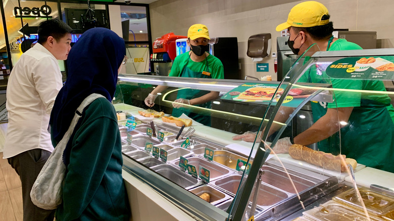 People ordering food from Subway employees.