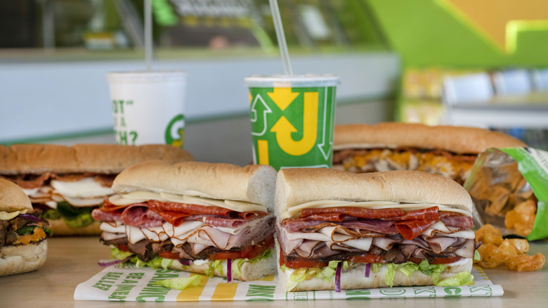 A subway sandwich cut in half with drinks, chips and other sandwiches in the background