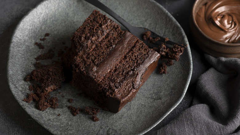 A slice of chocolate layer cake with a fork and chocolate sauce