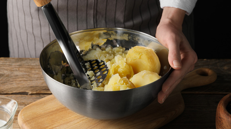 A chef mashes boiled potatoes in a bowl