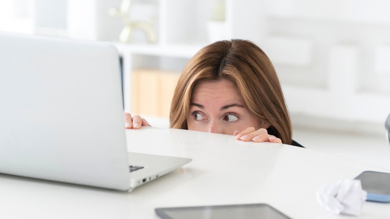 Person hiding behind desk and peering over at computer