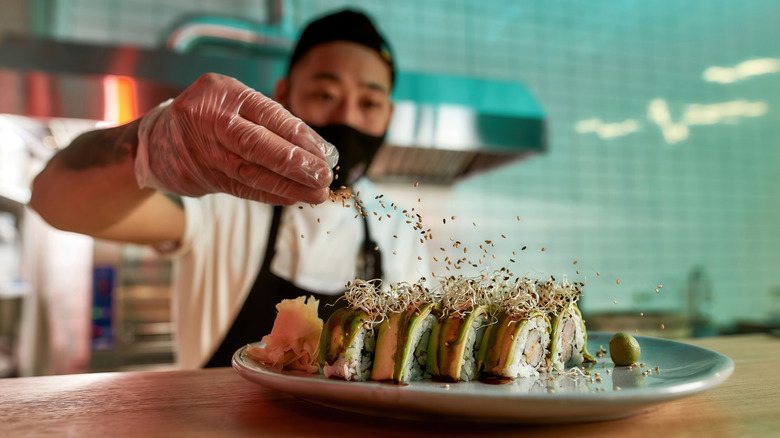 Chef sprinkles final touches on sushi roll