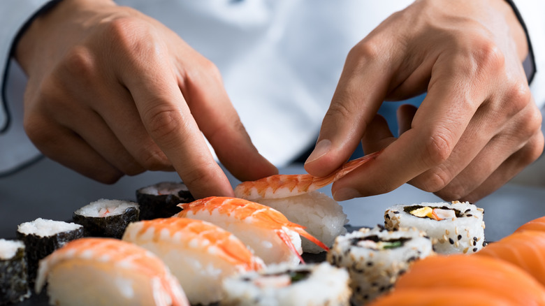 Chef's hands making nigiri roll by placing shrimp on rice