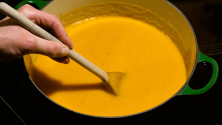 hand stirring creamy orange soup in a green pot with a wooden spoon