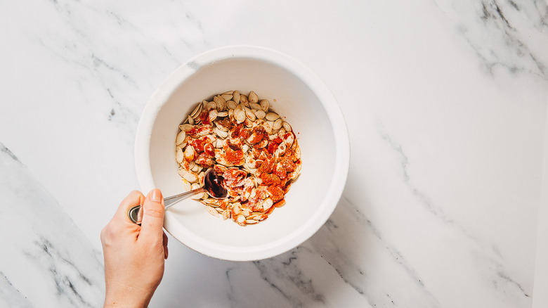 Hand stirring pumpkin seeds and seasonings in bowl