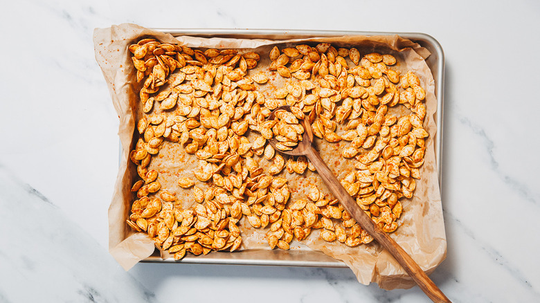 Seasoned pumpkin seeds spread out on baking sheet