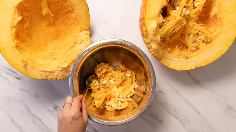Removing seeds from hollowed out pumpkin half to a bowl