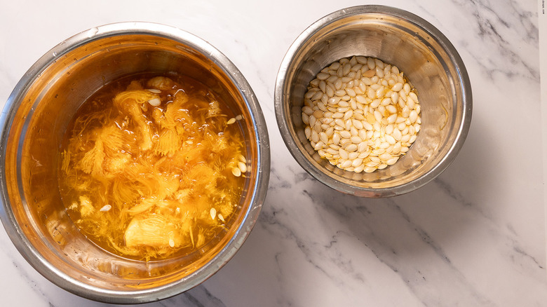 Pumpkin flesh in one bowl next to seeds in another