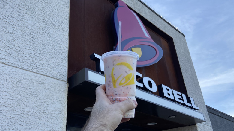hand holding Confetti Cookie Freeze in front of Taco Bell sign