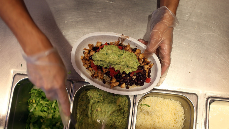 Top view of Chipotle employee spooning guacamole into a burrito bowl with rice, chicken, and black beans