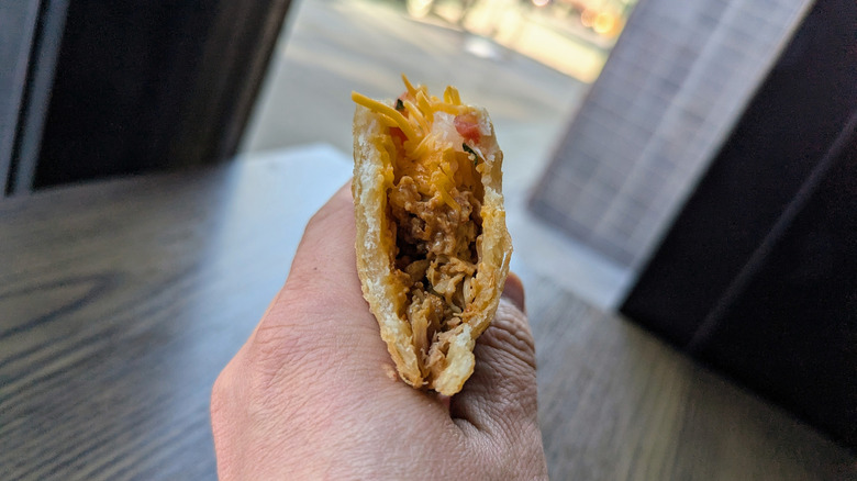 A hand holding a half-bitten Crispalupa from Taco Bell.