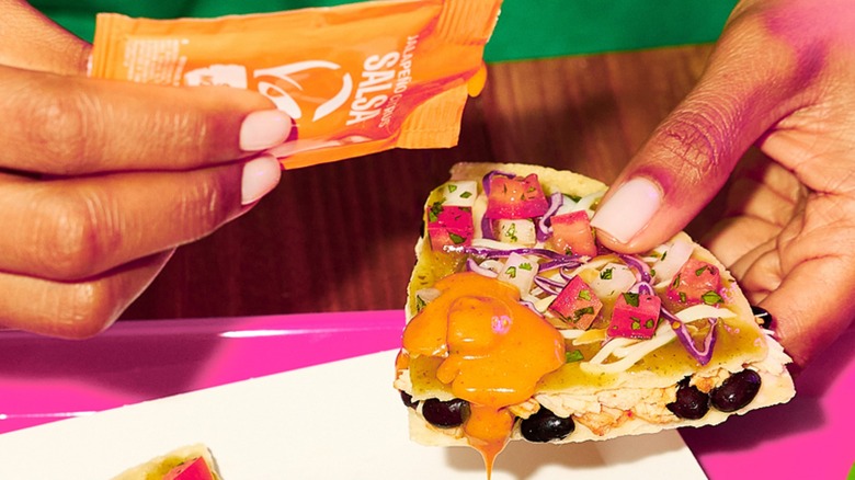 Person holding a piece of Taco Bell's Cantina Chicken Mexican Pizza and Jalapeño Citrus Salsa sauce packet
