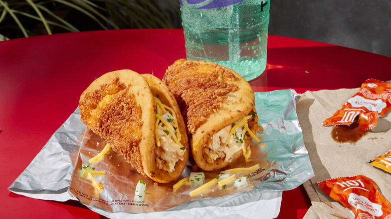 Two Taco Bell Toasted Cheddar Street Chalupas on foil wrapper with soda and sauce