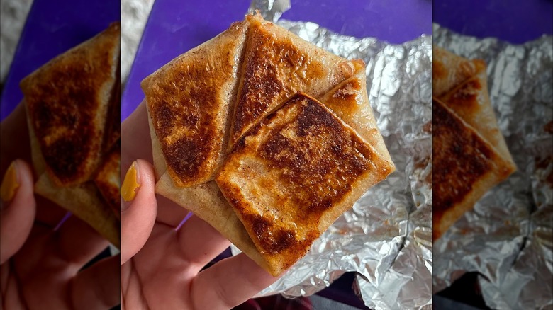 Hand holding Taco Bell's Crème Brûlée Crunchwrap Slider over foil