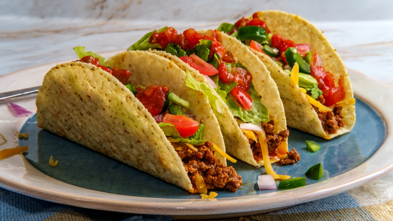 A plate of three crunchy tacos with ground beef, lettuce, tomatoes, and cheese