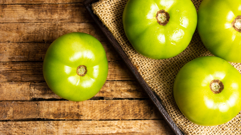 four green tomatoes sitting on a wooden surface