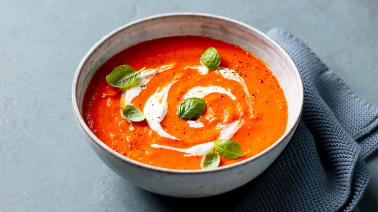 A bowl of tomato soup topped with cream and fresh basil