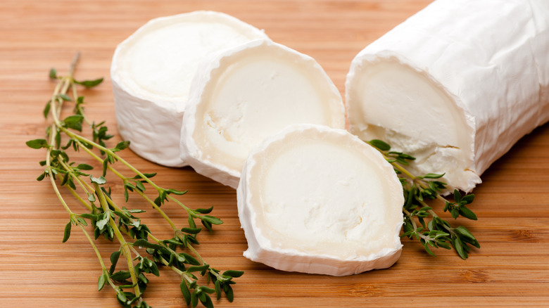 Sliced up goat cheese and thyme laying on a plain wooden cutting board.