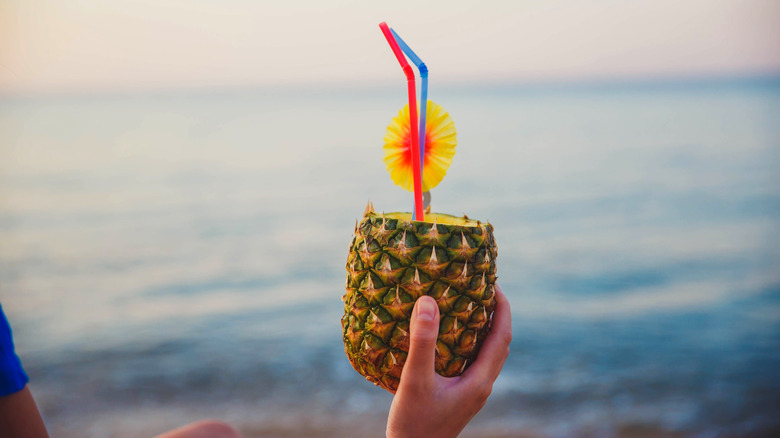 Person's hand holding a pineapple cocktail at the beach