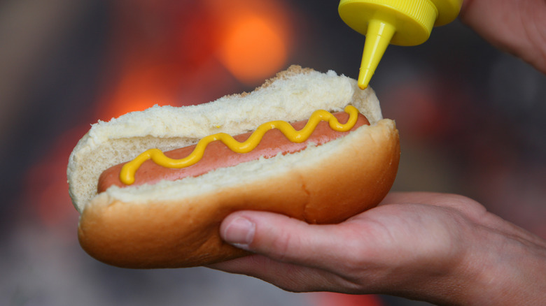 Someone putting mustard on a hot dog in a bun