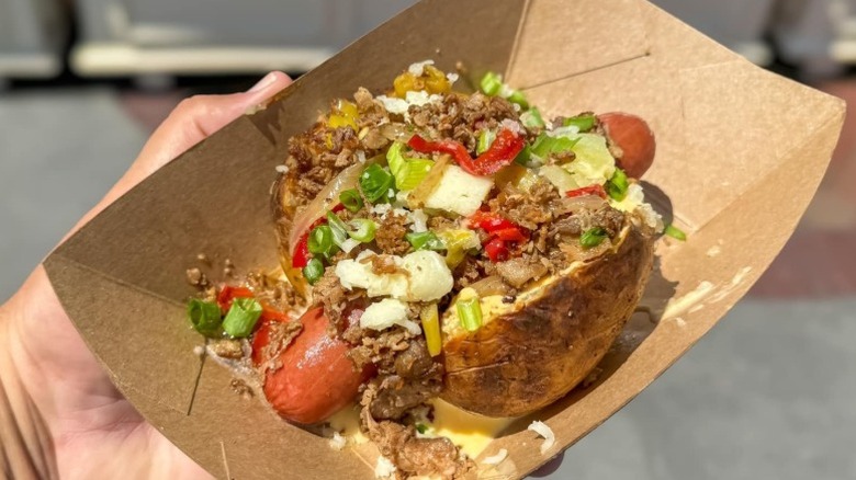 A hot dog in a baked potato bun with meat and veggie toppings