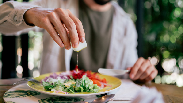 Person pouring olive oil on a salad