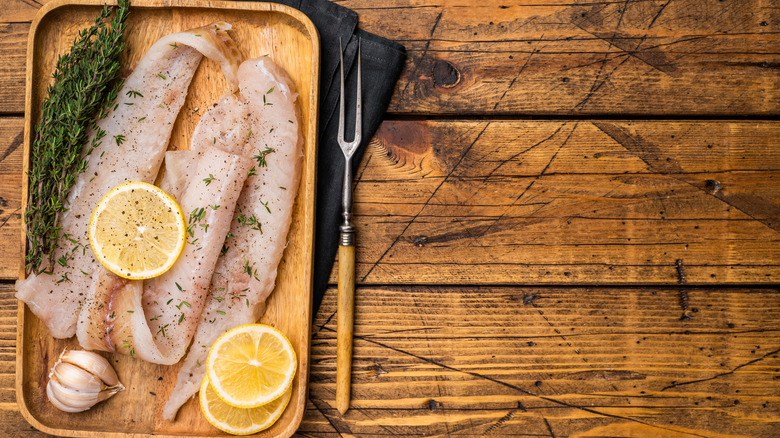 raw catfish fillets on a wood board with lemon slices, rosemary, and garlic