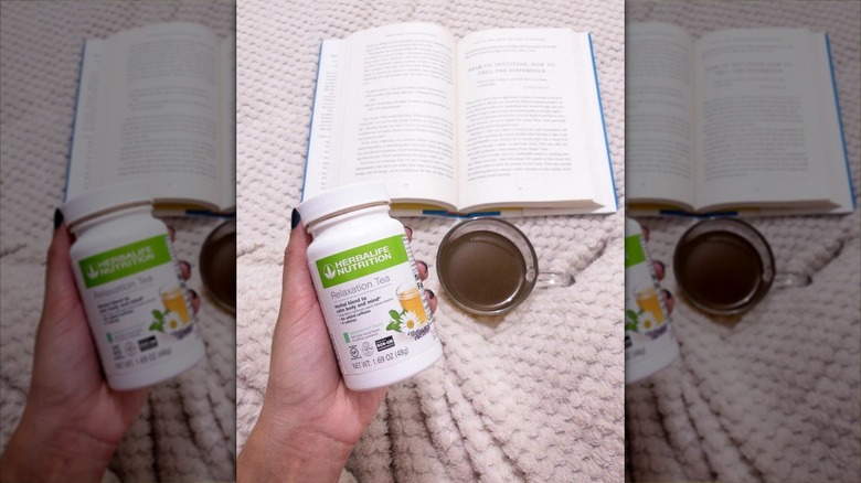Hand holding Herbalife Nutrition Relaxation Tea tub in bed