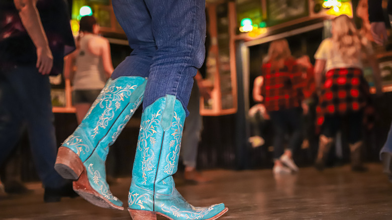 Someone wearing jeans and blue cowboy boots on a dance floor