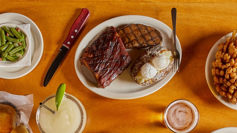 Plate of steak and baked potato with drinks at Texas Roadhouse
