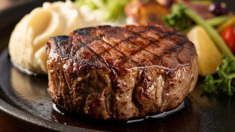 Grilled steak on black plate with sides in background
