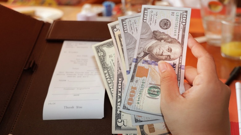 Person holding various denominations of dollar bills next to restaurant check