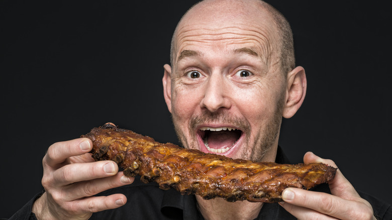 A smiling man holds a rack of ribs.