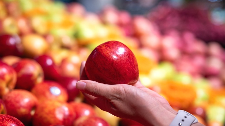 A shopper in the produce aisle of a supermarket holds a red apple.