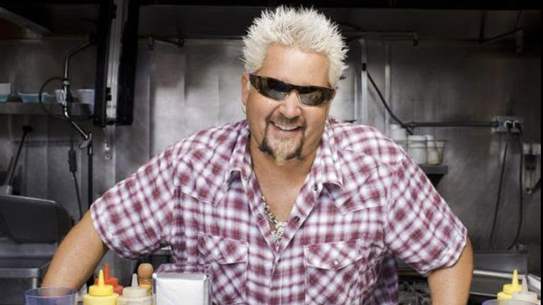 Guy Fieri wearing sunglasses and red and white shirt in a chef's kitchen