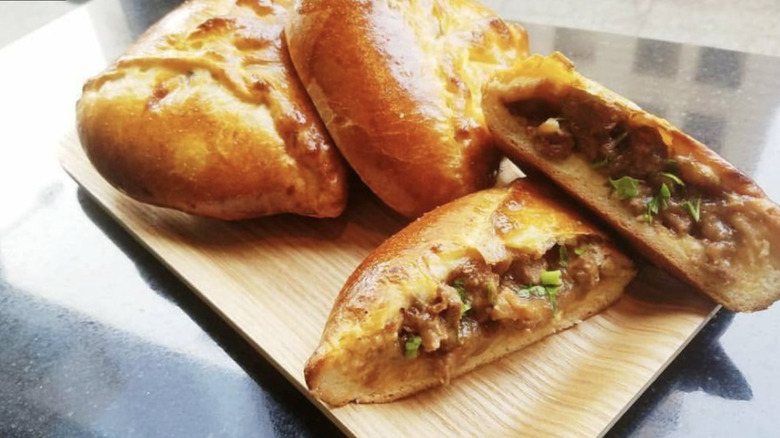 Pinoyshki's Piroshki with garlic beef asado cut open with two whole ones behind it on a wooden block