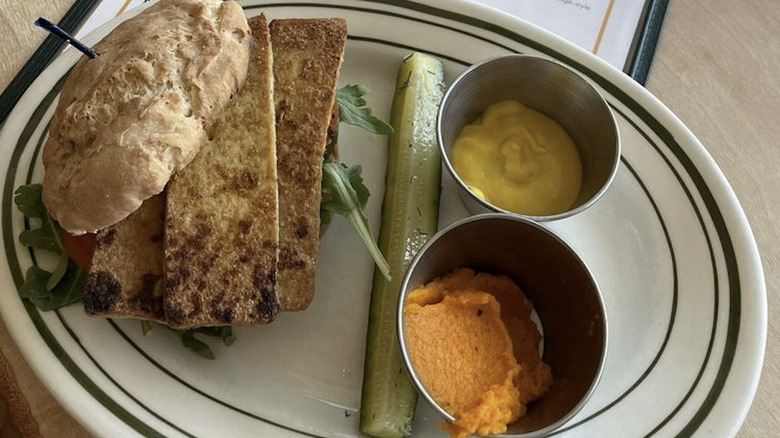 Tandem Bakery's Famers' Market Breakfast Sammie with pickle spear and dipping sauces on an oval white plate with a blue striped rim