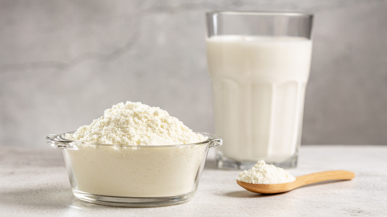 Bowl and spoon of powdered milk with glass of milk in the background