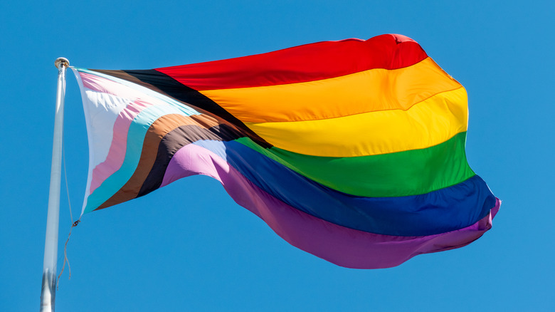 A pride flag on a flag pole blowing in the wind.