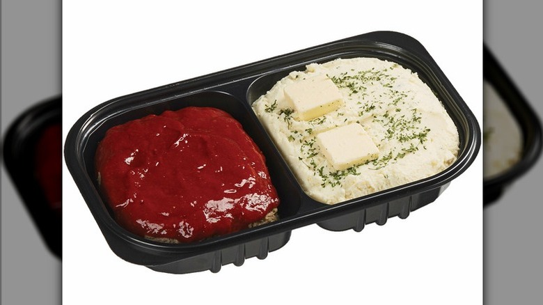 A plastic tray of meatloaf with ketchup and Yukon gold mashed potatoes with herbs and slabs of butter from Costco.