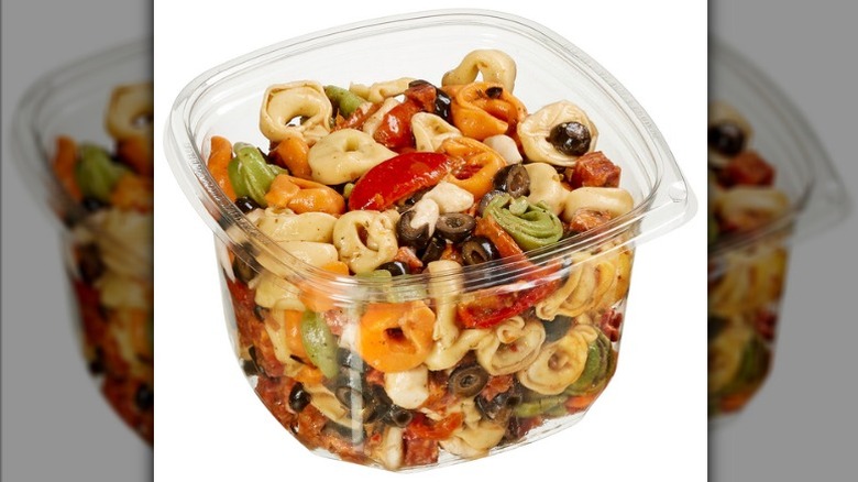 Plastic container of tortellini pasta salad from Costco's deli section with black olives and diced tomatoes