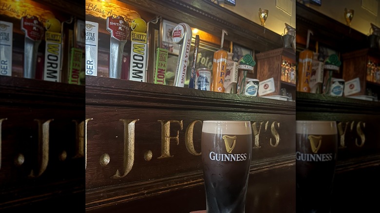 Freshly poured pint of Guinness on bartop in front of J.J. Foley's sign and row of beers on tap