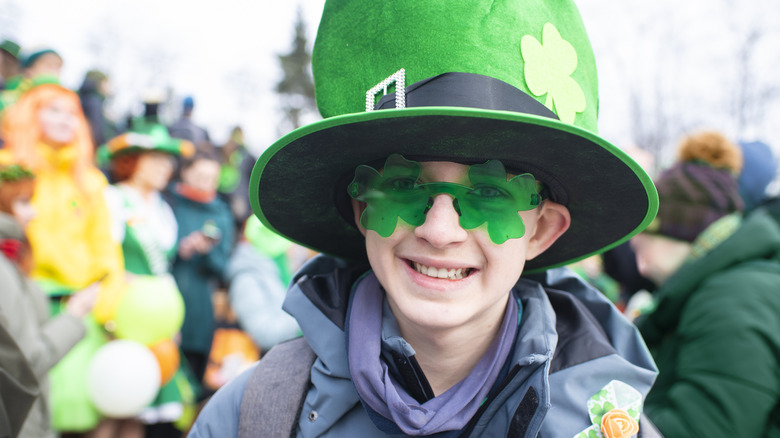 A boy wearing an oversized St Patrick's Day hat and shamrock glasses at a parade