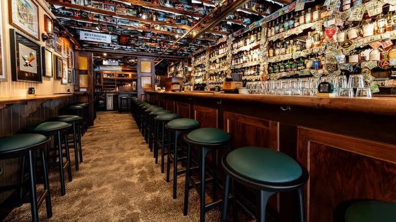 Empty interior of The Dead Rabbit bar in New York City, with bar stools lined up against counter in front of wall of liquor bottles
