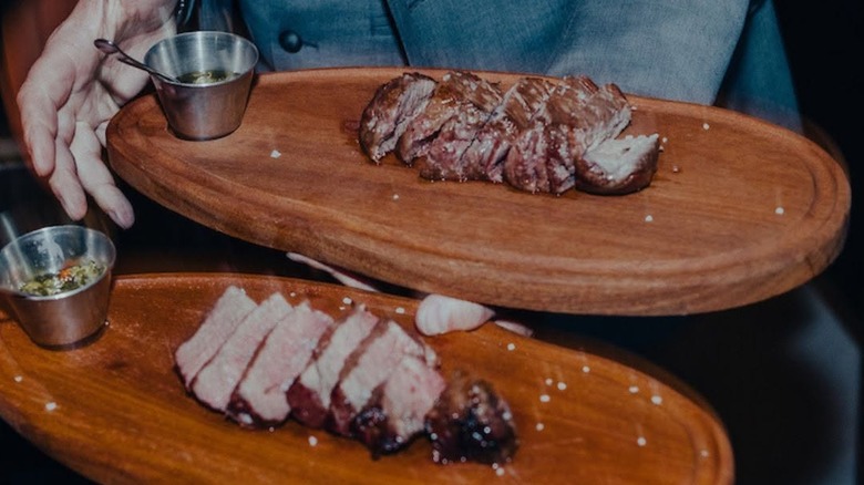 Person in suit carrying plates of meat at Fogo De Chão restaurant